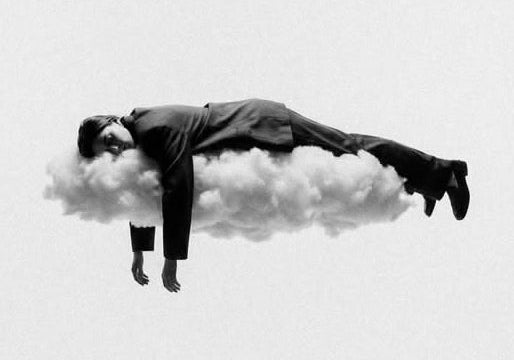 Minimalist black and white conceptual streetwear shot of a model floating on a cloud in a relaxed pose.